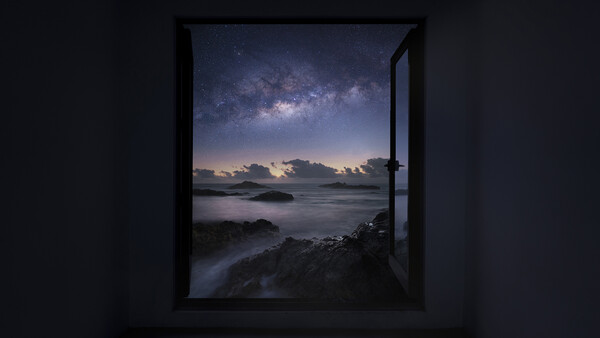 Open window framing a coastal night scene with the Milky Way visible in the starry sky above a calm sea.