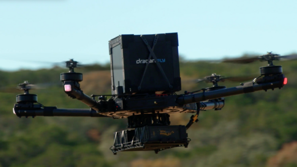 Large drone with extended arms and mounted camera equipment hovering over green landscape.