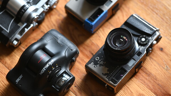 Collection of vintage rangefinder and SLR cameras arranged on a wooden surface.