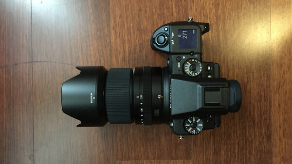 Mirrorless camera with attached lens and lens hood on wooden surface, overhead view.