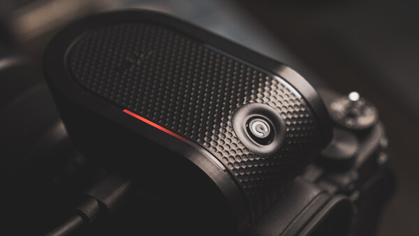 Close-up of a camera handgrip with textured black rubber surface and a red accent line.