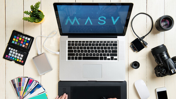 Overhead view of a photographer's workspace with laptop displaying MASV software, camera equipment, and color reference tools.