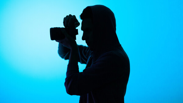 Silhouette of a photographer holding a camera up to their face against a bright blue background.