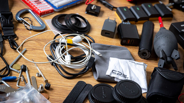 Photography gear and equipment organized on a wooden table, including headphones, cables, lens caps, and drone components.