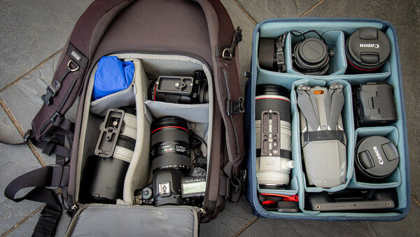 Photography gear organized in a burgundy backpack and blue storage insert, including camera body, lenses, and accessories.