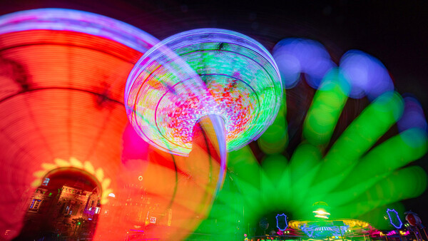 Nighttime carnival or fair scene with glowing red Ferris wheel on left and neon green inflatable structures on right against dark sky.