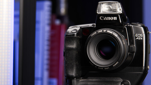 Canon EOS 1V film camera with battery grip attached, positioned against blurred blue and dark background.