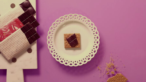 Styled flat lay with chocolate squares on a decorative plate and wrapped candies on a split pink and cream background.