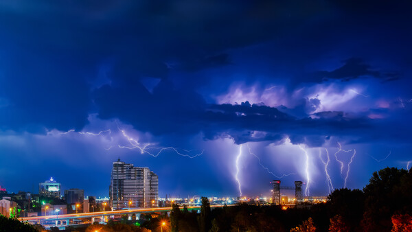 Thunderstorm with multiple lightning bolts striking over an illuminated city skyline at night.