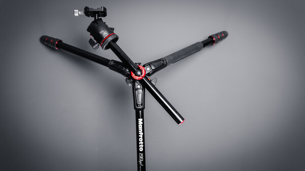 Professional tripod with three extended legs and ball head with smartphone mount against gray background.