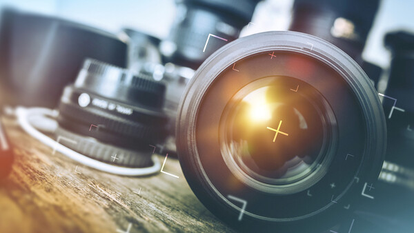 Multiple camera lenses arranged on a wooden surface with golden hour sunlight reflecting off the front element of the closest lens.