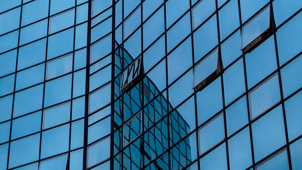 Modern glass skyscraper facade with geometric grid pattern and reflective building silhouette.