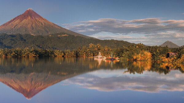 Conical volcano with perfect mirror reflection in still lake at golden hour.