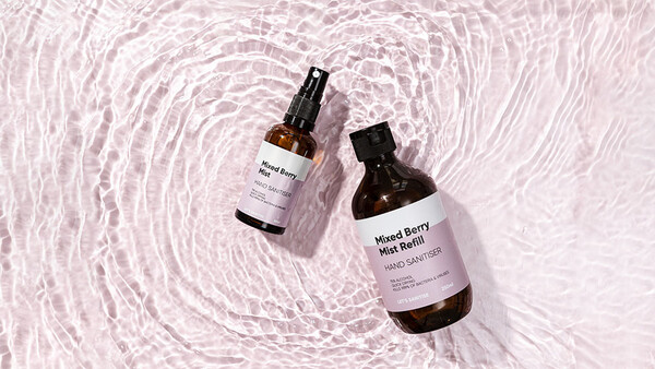 Two dark glass bottles with spray tops positioned on rippled water surface with soft shadows.