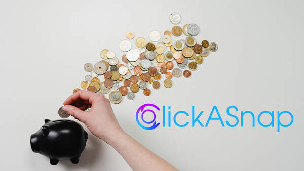 Hand dropping coins into a black piggy bank with coins scattered above on white background.