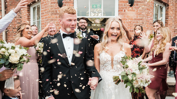 Newlyweds walk together while guests throw gold confetti during outdoor wedding recessional.