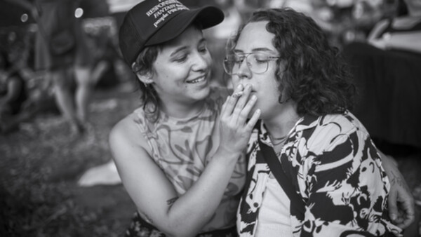 Two people laughing together outdoors in black and white, one wearing a baseball cap and patterned shirt.