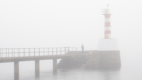 Lighthouse and pier shrouded in thick fog, minimalist coastal scene.