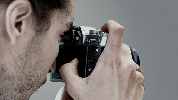 Photographer holding a mirrorless camera up to his eye while composing a shot.