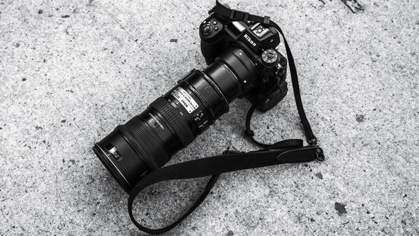 Professional DSLR camera with telephoto lens on concrete surface with neck strap.
