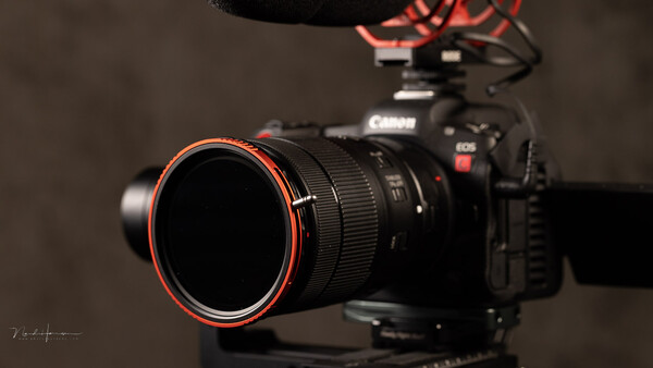 Canon EOS R5C mirrorless camera with Canon lens featuring red accent ring, mounted on tripod with directional microphone visible above.