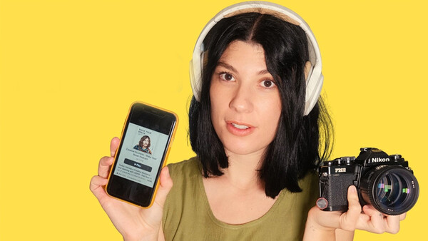 Woman holding smartphone and vintage Nikon camera against yellow background.