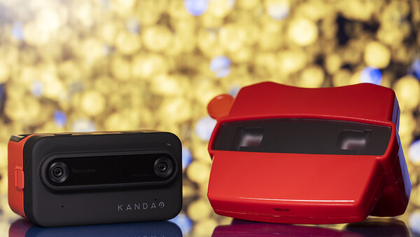 Two compact dual-lens camera devices displayed against a blurred golden bokeh background.