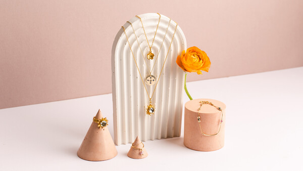 Minimalist still life with arched white sculptural form, peach ceramic vessels, and yellow flower against pink and white background.