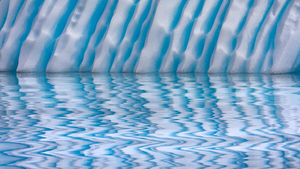 Underwater view of a swimming pool with rippling water surface and blue lane dividers reflecting light.