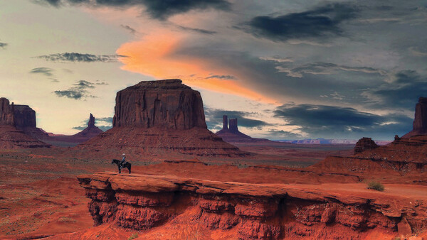 Desert landscape at sunset with rock formations and a lone horseback rider in the foreground.