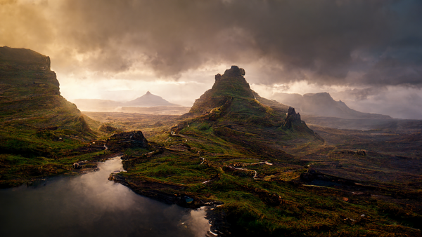 Dramatic landscape with moss-covered peaks, a winding road, and moody storm clouds breaking into golden light.