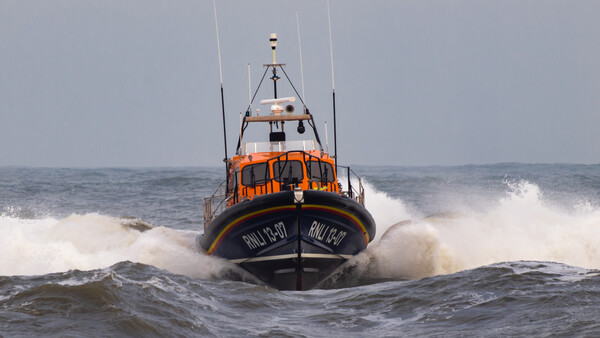 Orange and blue lifeboat navigating through large white-capped waves in rough ocean conditions.