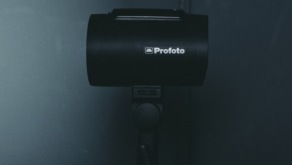 Profoto studio flash head mounted on a stand against a dark gray background.