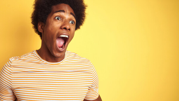 Young man with afro hair sticking out tongue against bright yellow background.