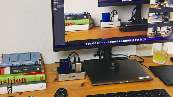 Creative workspace with monitor displaying editing software, desk accessories, and stacked books on wooden surface.