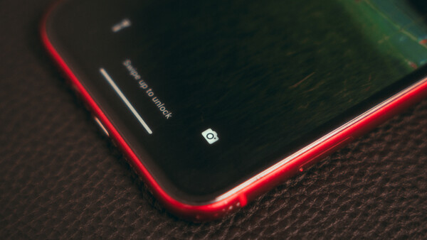 Red smartphone with dark screen on textured fabric surface, showing camera icon and notification indicators.