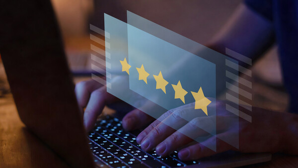 Hands typing on a laptop keyboard with a glowing five-star rating graphic floating above the screen.