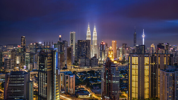 Illuminated city skyline at dusk with twin towers and dense high-rise buildings.