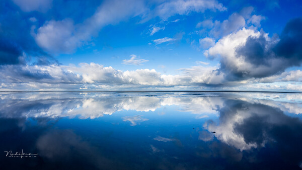 Perfectly mirrored sky and clouds reflected in still water at horizon line.