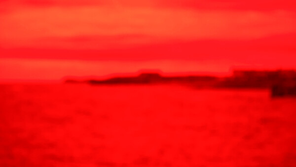 Blurred landscape with red-toned sky and dark landforms along the horizon.