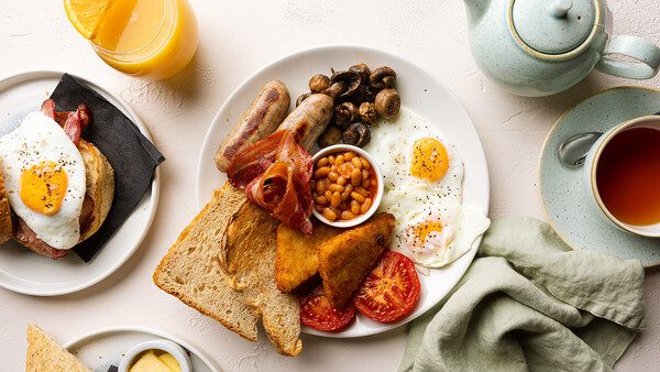Overhead flat lay of a full breakfast spread with eggs, bacon, toast, and fresh fruit on white plates.