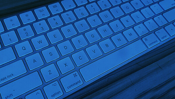Backlit laptop keyboard illuminated in blue with shallow depth of field.