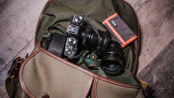 Mirrorless camera with attached lens inside a canvas and leather camera bag on a wooden surface.