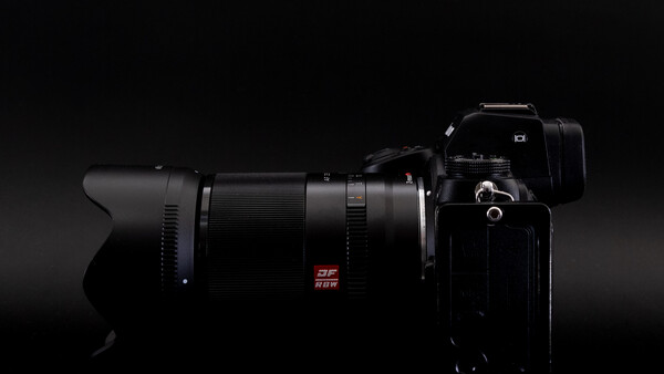 Professional camera with telephoto lens mounted, positioned against a dark background with dramatic side lighting.
