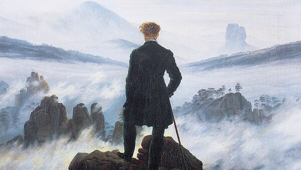 Man in dark coat standing on rocky outcrop overlooking misty mountain valley.