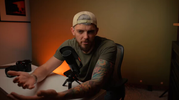 Male content creator seated at desk with studio microphone and warm orange lighting setup.