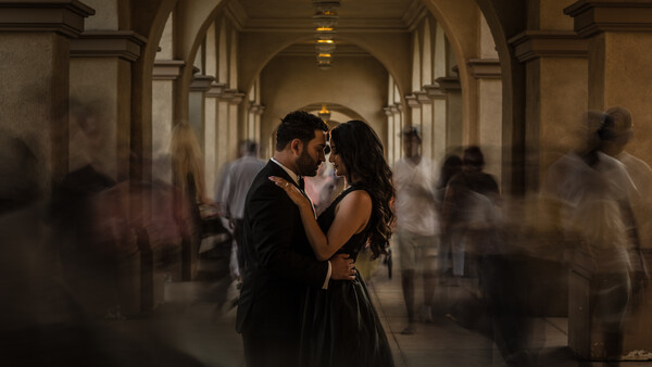Couple kissing in an arched stone corridor surrounded by motion-blurred figures.