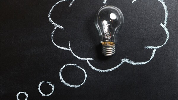 Incandescent light bulb centered in chalk-drawn cloud shapes on dark chalkboard surface.