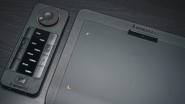 Drone remote controller with joystick and button panel displayed on dark surface next to tablet.