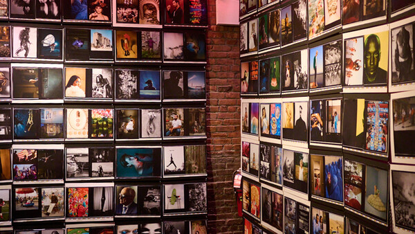 Gallery wall displaying hundreds of framed photographs and artwork arranged in a grid pattern across exposed brick.